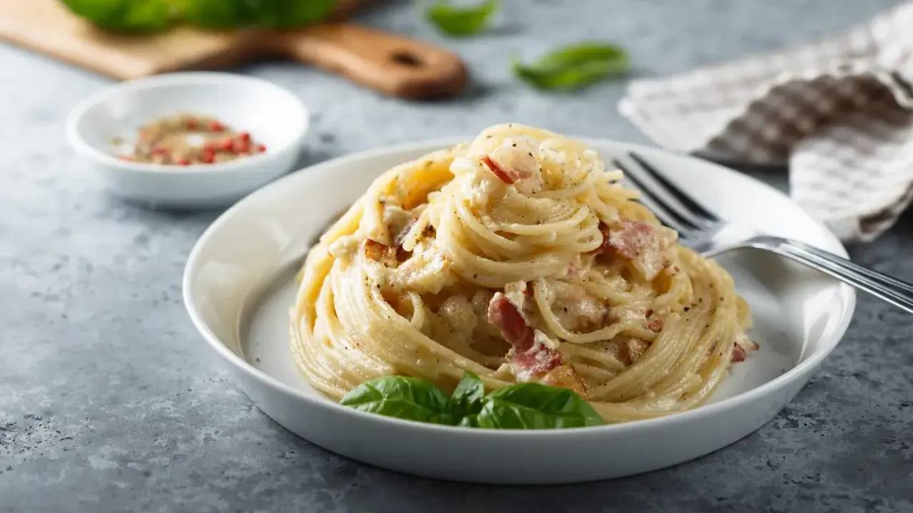 Un piatto di spaghetti alla carbonara, perfetto per la giornata della carbonara, guarnito con basilico fresco.