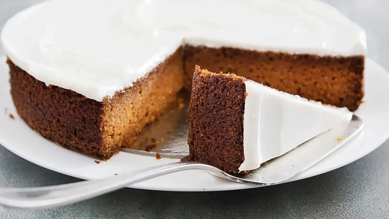 Una fetta di torta di carote e yogurt, soffice e ricoperta di glassa bianca, pronta per essere gustata.