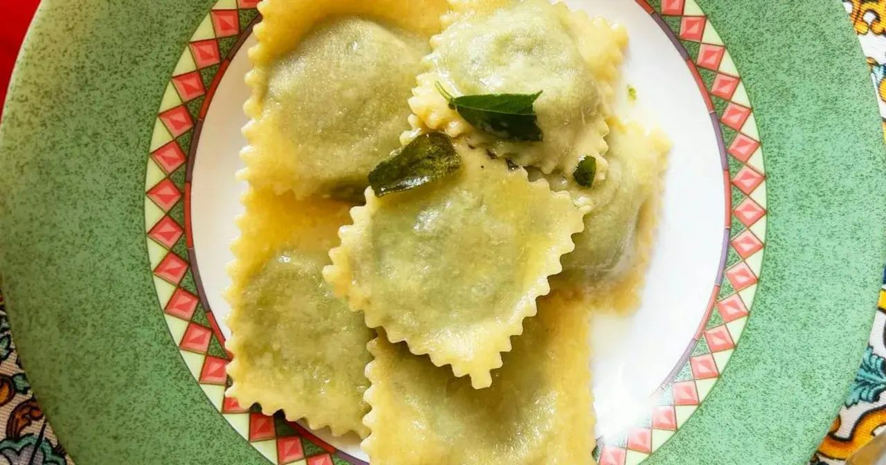 Ravioli ricotta e spinaci conditi con burro fuso e salvia, serviti su un piatto decorato.