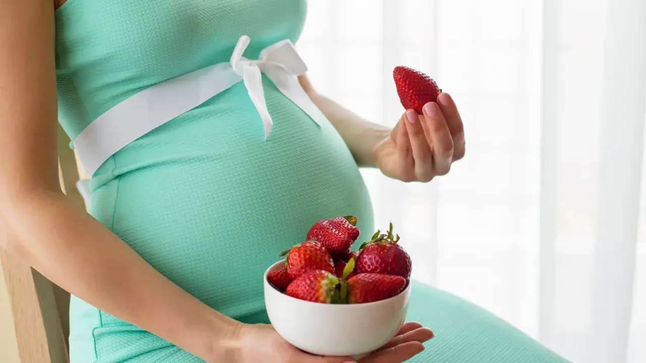 Pancione e fragole, un dolce desiderio in gravidanza. La futura mamma tiene una fragola in mano e una ciotola piena.
