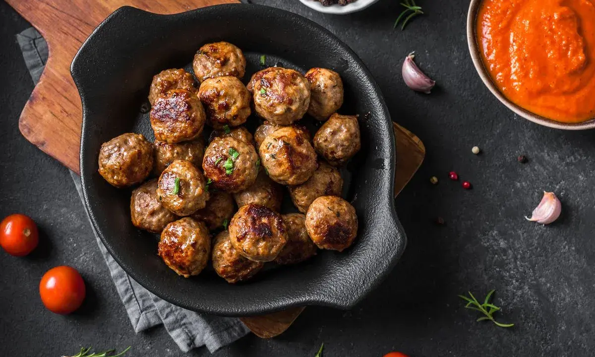 Polpette dorate e succulente, appena sfornate dalla friggitrice ad aria, pronte per essere gustate con salsa e pomodorini freschi.