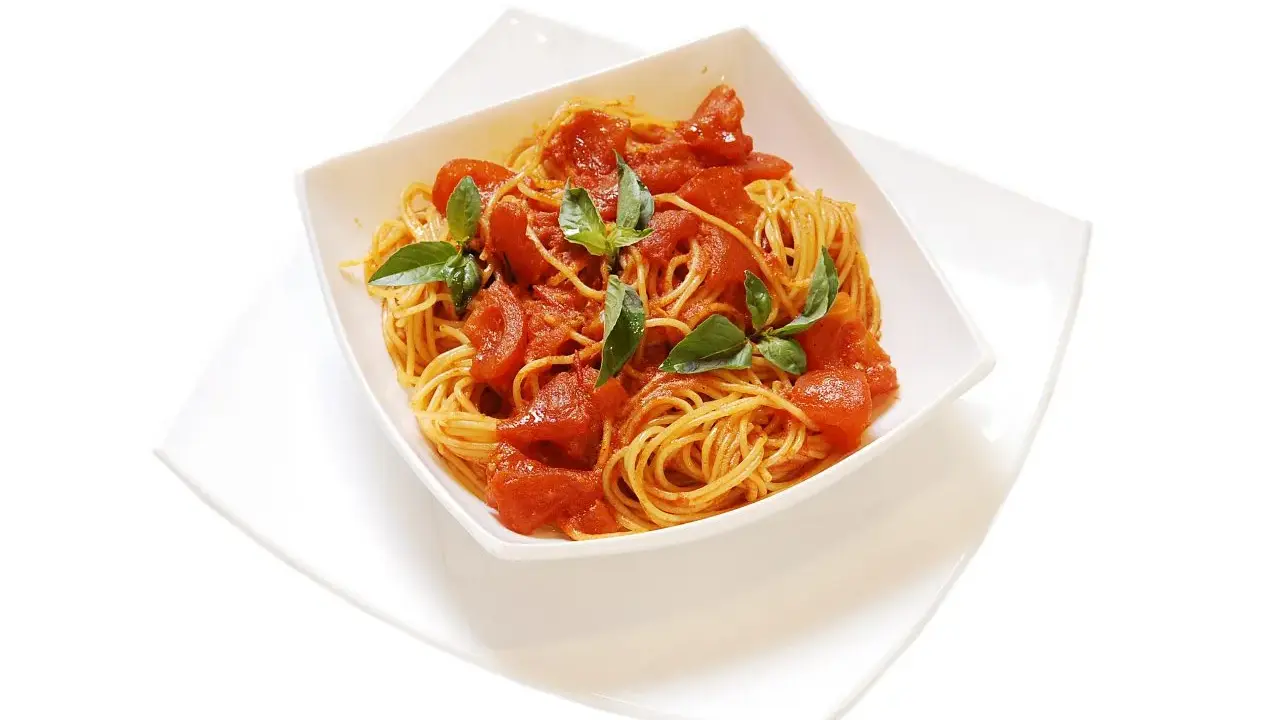 Un invitante piatto di spaghetti al pomodoro fresco, guarnito con foglie di basilico verde brillante.