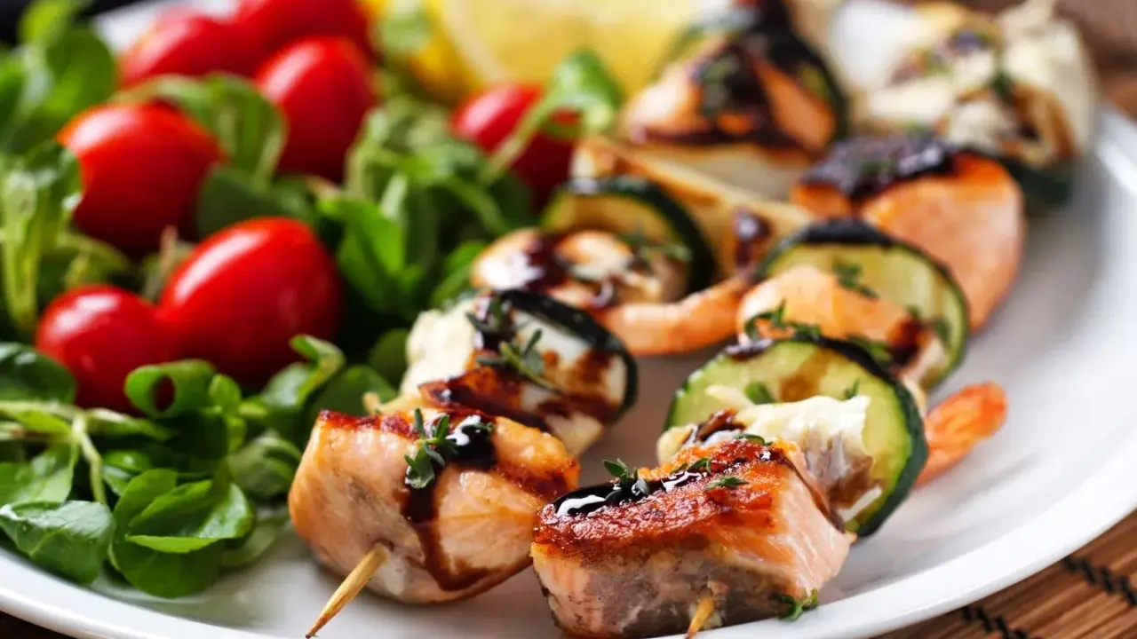 Spiedini di pesce succulenti con salmone, gamberi e zucchine, guarniti con erbe aromatiche e salsa, serviti con insalata fresca e pomodorini.