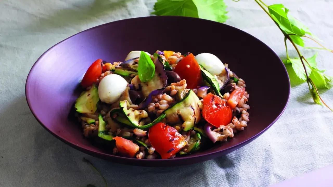 Insalata di farro estiva con verdure grigliate, pomodorini, mozzarelline e basilico, un piatto fresco e colorato.