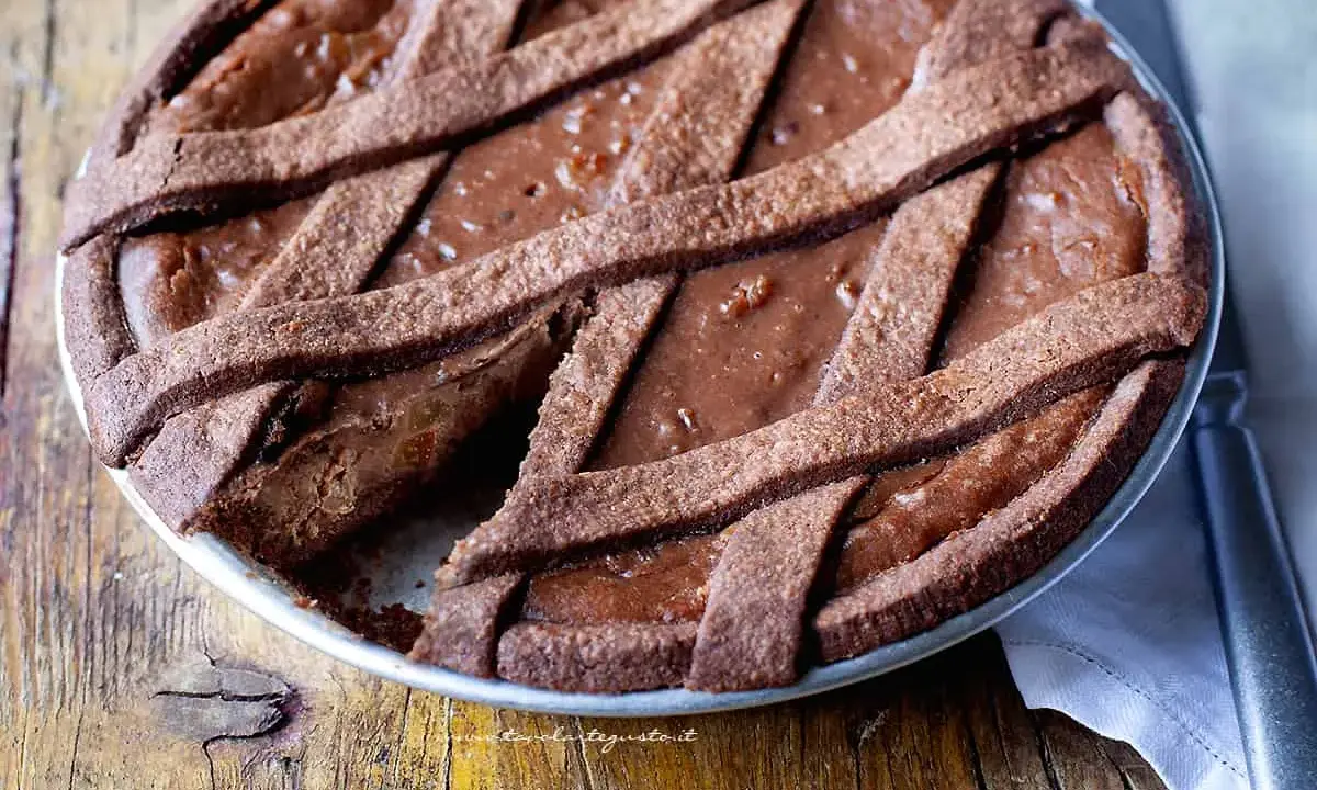 Pastiera al cioccolato con scorze candite, un dolce goloso su un tavolo di legno rustico.