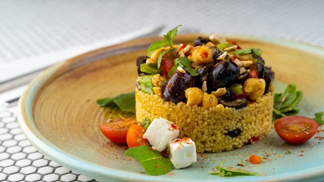 Cous cous condito con olive, ceci, pomodorini e feta. Un'idea gustosa su come condire il cous cous per un piatto colorato e saporito.