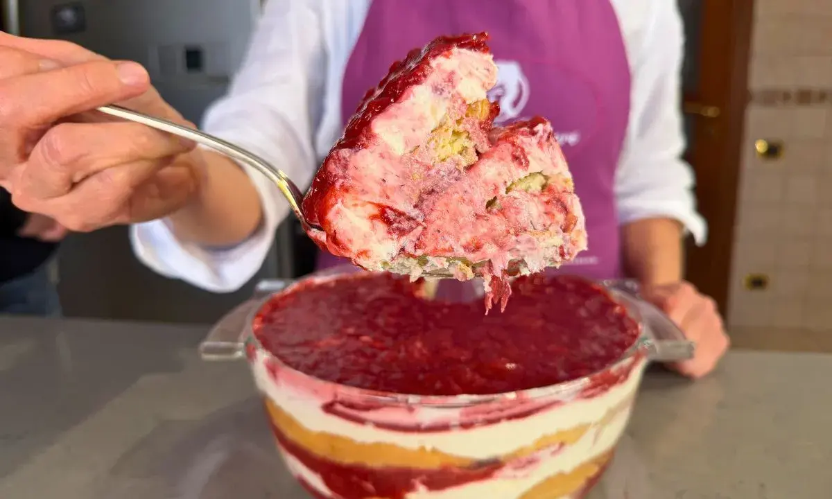Un cucchiaio solleva una porzione generosa di un goloso tiramisù alle fragole, stratificato con crema e biscotti, pronto per essere gustato.