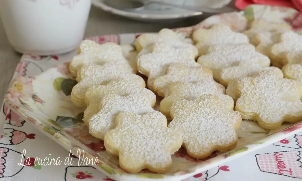 Deliziosi biscotti al burro a forma di fiore, spolverati di zucchero a velo, su un vassoio floreale.