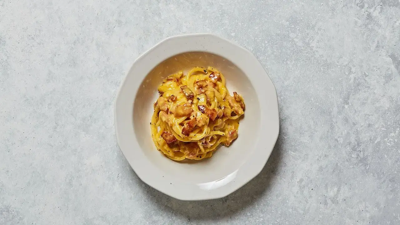 Un piatto di spaghetti alla carbonara, con il suo guanciale croccante e la crema d'uovo e pecorino, pronto per essere gustato.