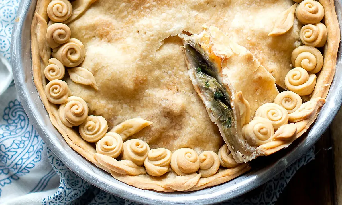 Torta salata con carciofi, decorata con rose di pasta frolla e foglie, pronta per essere gustata.
