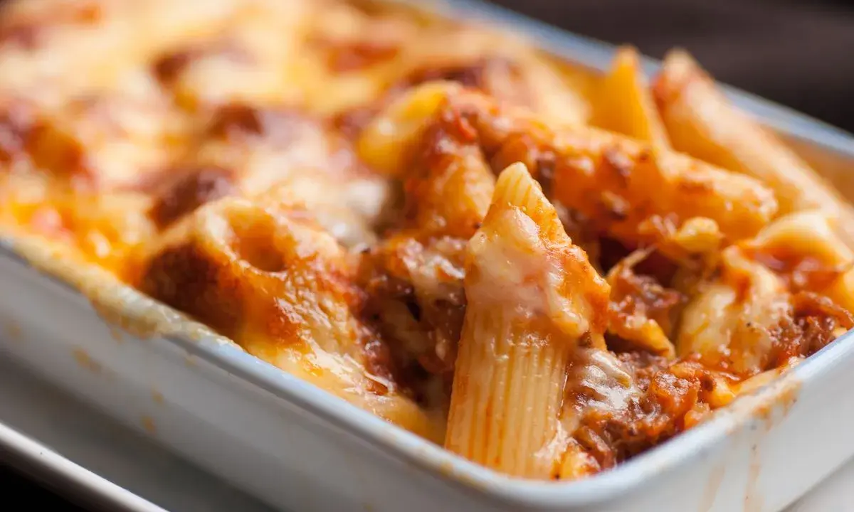 Piatto fumante di pasta pasticciata al forno, con penne ricoperte di sugo e formaggio fuso.
