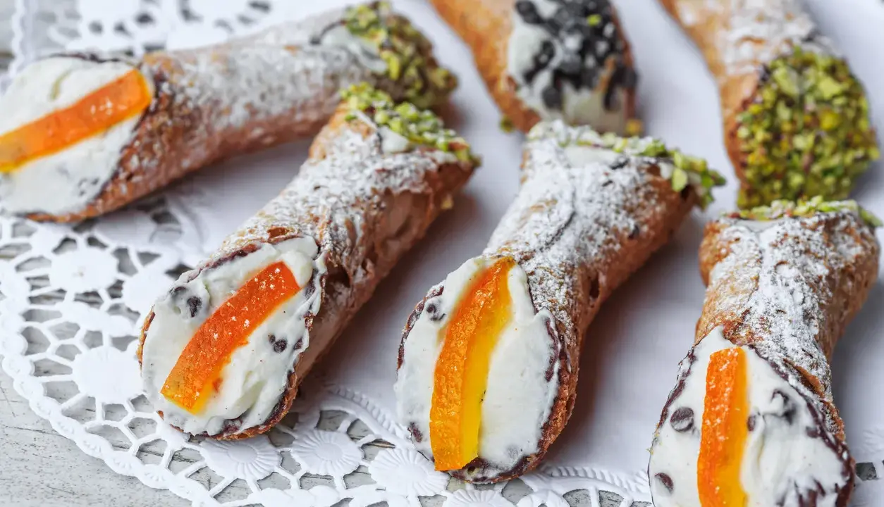 Cannoli siciliani, dolci tipici con crema e canditi, spolverati di zucchero a velo e guarniti con pistacchi o gocce di cioccolato.