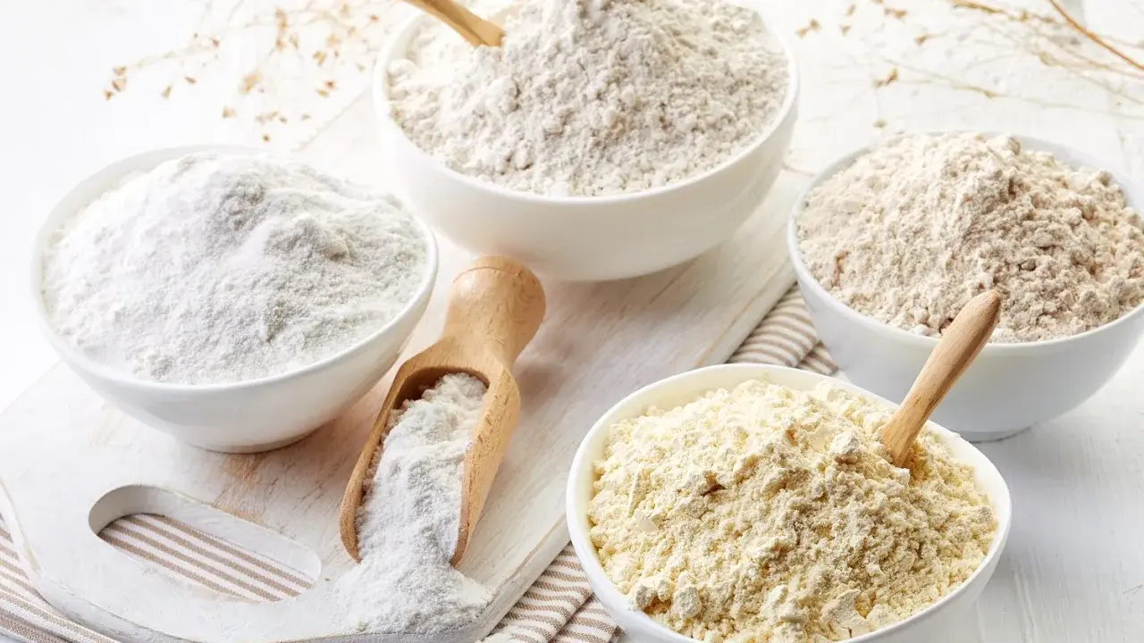 Diverse ciotole mostrano vari tipi di farina, da quella bianca finissima a quelle più grezze e giallastre, pronte per ogni ricetta.
