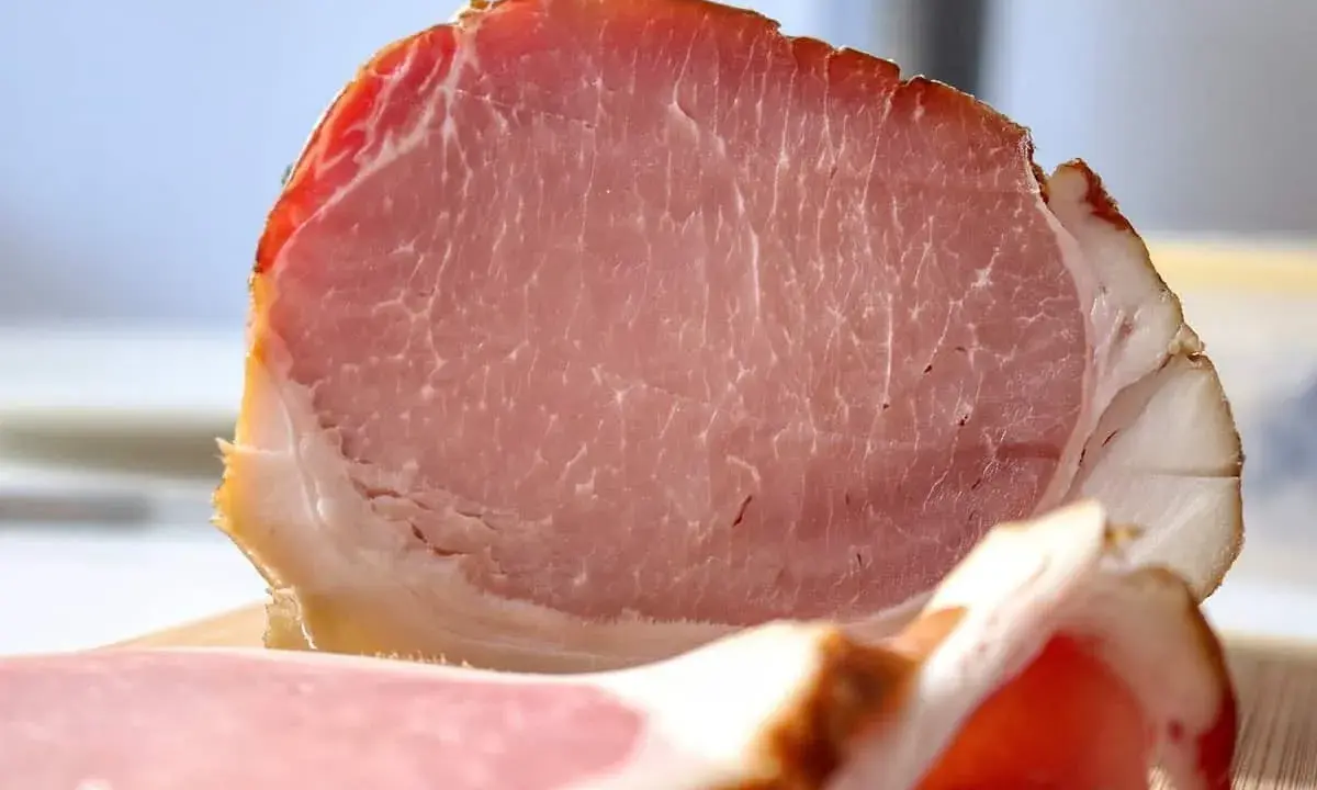 Fetta di prosciutto cotto, un insaccato rosa con striature di grasso bianco e un bordo dorato.