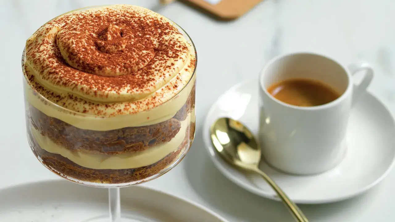 Delizioso tiramisù senza caffè, stratificato con crema e cacao, accanto a un espresso.