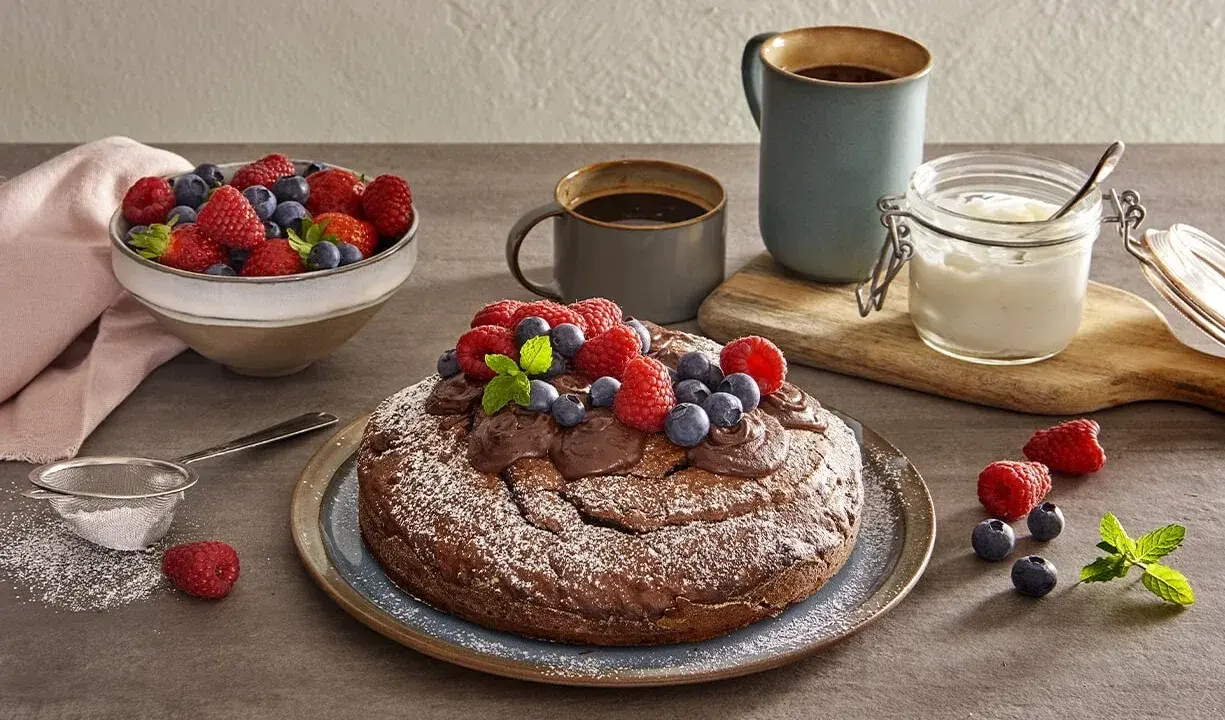 Torta yogurt e cioccolato, cosparsa di zucchero a velo e decorata con frutti di bosco freschi, pronta per essere gustata con un caffè.