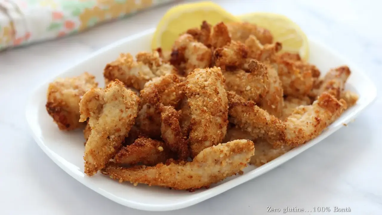 Straccetti di pollo croccanti in friggitrice ad aria, serviti con spicchi di limone.