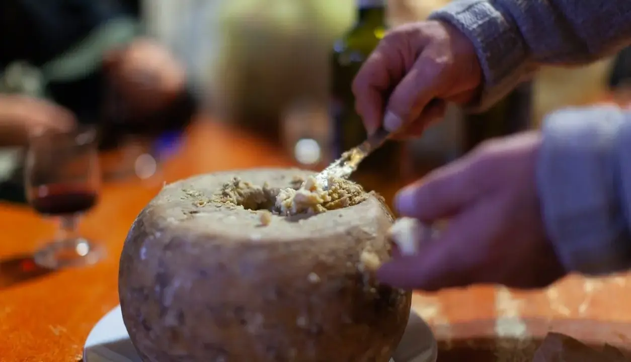 Un uomo serve un formaggio con i vermi, una specialità sarda, con un coltello. Sul tavolo, un bicchiere di vino rosso.