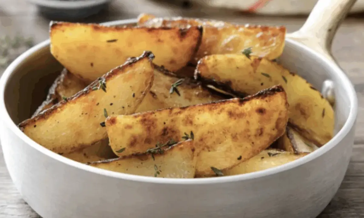 Patate in padella dorate e croccanti, condite con erbe aromatiche, servite in una ciotola bianca.