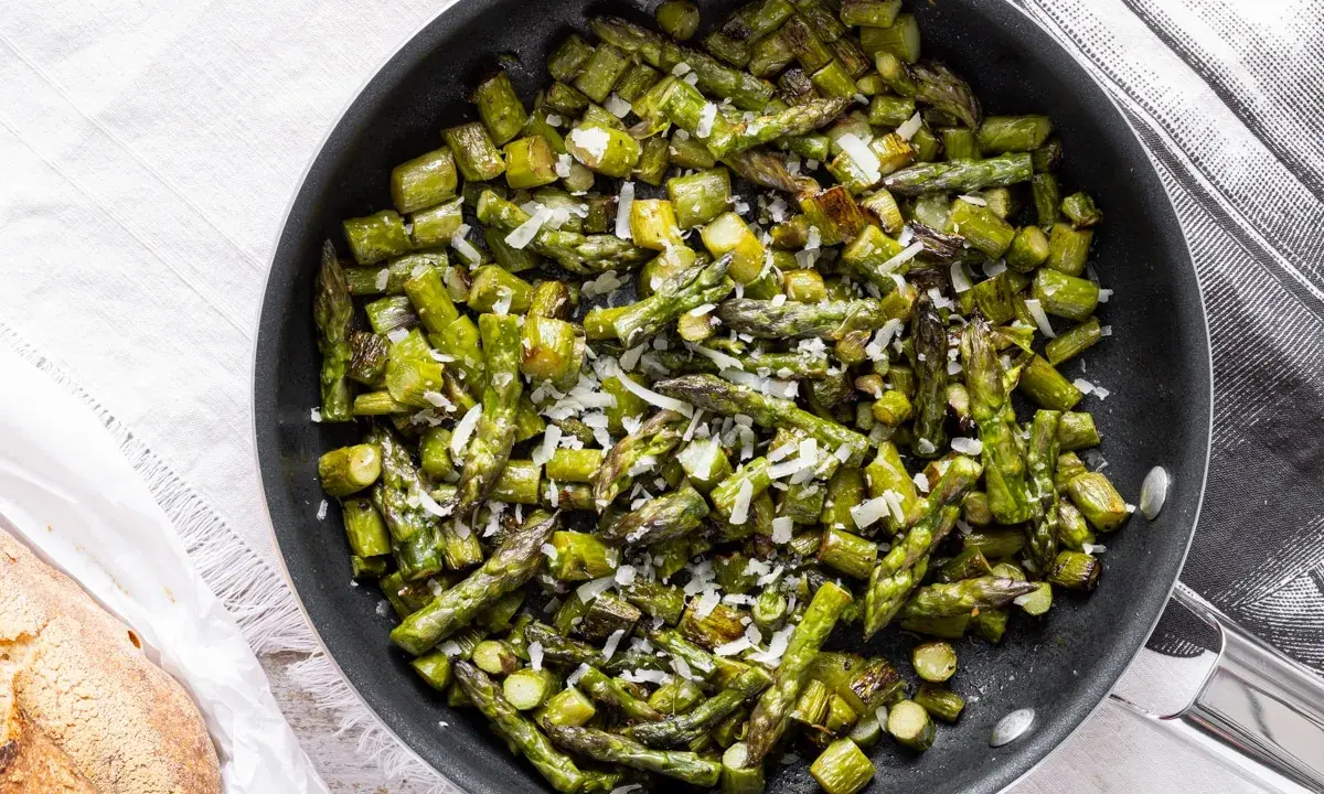 Asparagi in padella, saltati e cosparsi di parmigiano grattugiato, pronti per essere gustati.