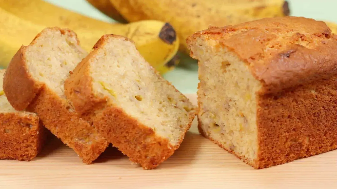 Fette di banana bread light, soffice e dorato, con banane mature sullo sfondo.