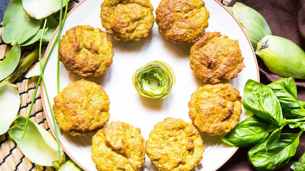 Muffin dorati, perfetti per una colazione proteica salata. Circondati da carciofi e basilico fresco, invitano a un pasto nutriente.