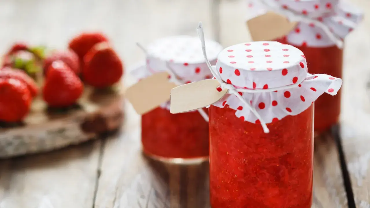 Barattoli di marmellata di fragole fatti in casa, con fragole fresche sullo sfondo.
