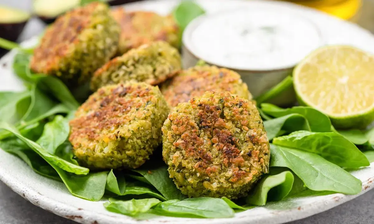 Polpette di spinaci dorate su un letto di spinaci freschi, con una ciotolina di salsa e spicchi di lime.