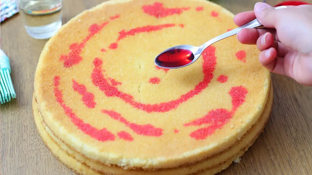Un cucchiaino di sciroppo rosso viene versato su un pan di spagna decorato con un motivo a spirale. La bagna per pan di spagna renderà la torta più umida e saporita.