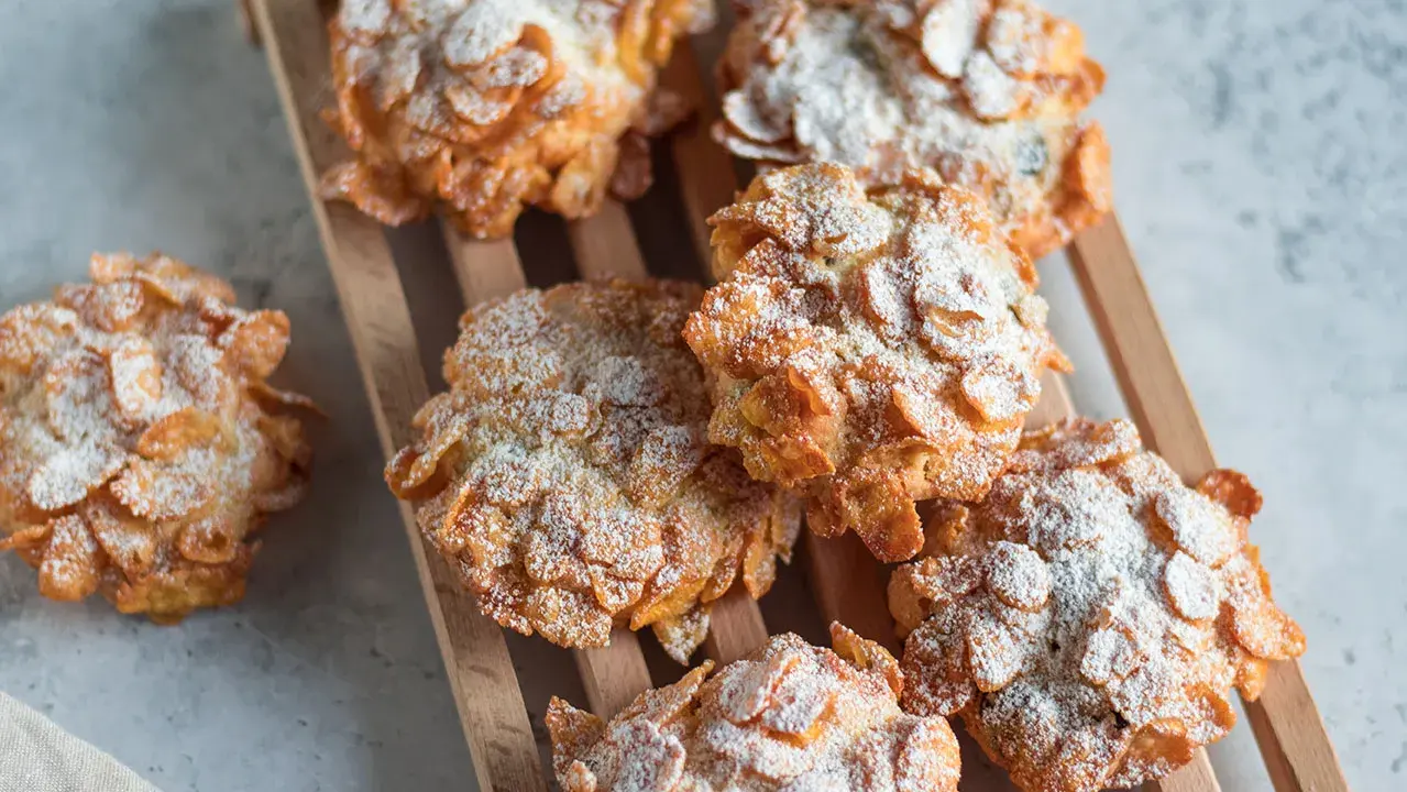 Dolci croccanti, simili a rose del deserto, ricoperti di fiocchi di mais e spolverati di zucchero a velo.