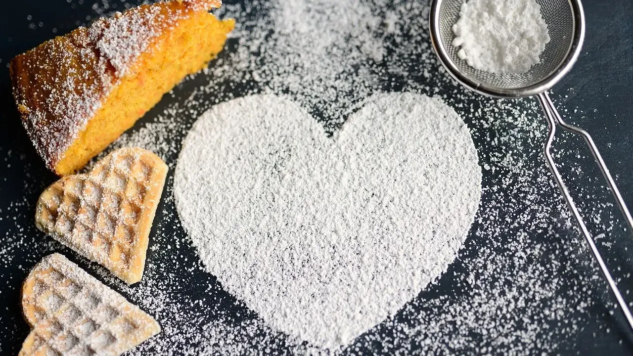 Un cuore di zucchero a velo, un pezzo di torta arancione e due biscotti a forma di cuore. Ecco come fare lo zucchero a velo per decorare dolci.