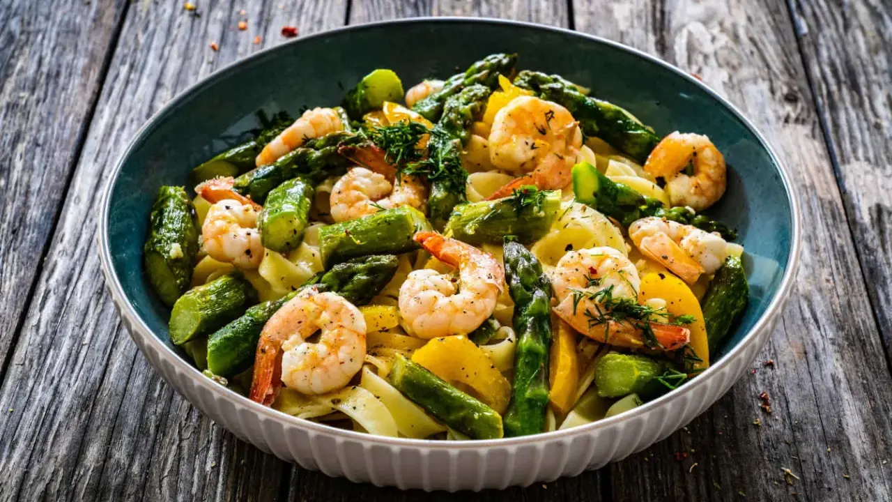 Un piatto invitante di pasta con asparagi e gamberetti, condito con erbe fresche e servito su un tavolo di legno rustico.