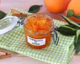 Barattolo di marmellata di arance fatto in casa, con arance fresche e bastoncini di cannella sullo sfondo.
