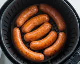 Sette salsicce dorate e succulente cuociono nella friggitrice ad aria, pronte per essere gustate.