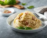 Un piatto di spaghetti alla carbonara, perfetto per la giornata della carbonara, guarnito con basilico fresco.