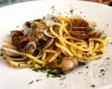 Spaghetti con lupini di mare, un piatto di pasta fresca condita con molluschi e prezzemolo tritato, servito su un piatto bianco.