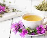 Una tazza di tisana alla malva, decorata con fiori viola, pronta a donare i suoi benefici.