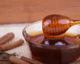 Miele di castagno, ricco di proprietà benefiche, gocciola da un cucchiaio in una ciotola. Cannella e polvere scura completano la scena.