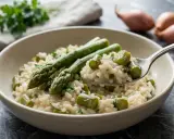 Un cremoso risotto con asparagi freschi, guarnito con prezzemolo tritato. Una forchettata mostra la consistenza perfetta.