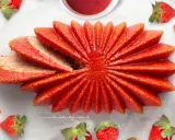 Delizioso dolce a forma di fiore, con fette di torta alle fragole che si aprono come petali. Fresche fragole circondano questo dolce, invitando a gustare la sua dolcezza.