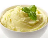 Una ciotola bianca piena di soffice crema di patate, guarnita con foglie di basilico fresco.