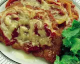 Cotoletta alla bolognese ricoperta di sugo e formaggio fuso, servita con insalata fresca su un piatto decorato.