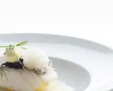 Piatto gourmet con filetto di pesce bianco, crema gialla, erbe aromatiche e fili croccanti. Un'interpretazione moderna che evoca la differenza tra baccalà e stoccafisso.
