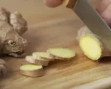 Un pezzo di zenzero fresco viene affettato su un tagliere di legno, mostrando come si mangia questo ingrediente versatile.