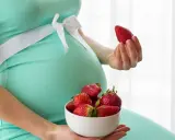 Pancione e fragole, un dolce desiderio in gravidanza. La futura mamma tiene una fragola in mano e una ciotola piena.