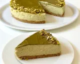Una fetta di goloso cheesecake al pistacchio, con la torta intera sullo sfondo, decorata con granella di pistacchi.