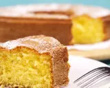 Una fetta di torta 7 vasetti soffice e dorata, cosparsa di zucchero a velo, su un piatto bianco con una forchetta.