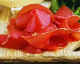 Fette sottili di bresaola, un insaccato di manzo stagionato, disposte su un tagliere di legno con pane e prezzemolo sullo sfondo.