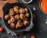Polpette dorate e succulente, appena sfornate dalla friggitrice ad aria, pronte per essere gustate con salsa e pomodorini freschi.