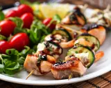Spiedini di pesce succulenti con salmone, gamberi e zucchine, guarniti con erbe aromatiche e salsa, serviti con insalata fresca e pomodorini.